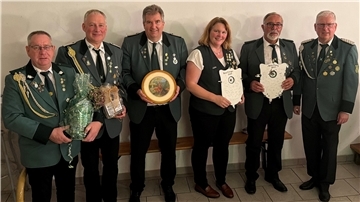 Sechs Mitglieder des Schützenvereins in grünen Uniformjacken stehen nebeneinander und präsentieren ihre Auszeichnungen. Zwei Personen halten bemalte Holzscheiben, andere haben Geschenke in den Händen.