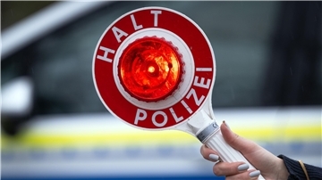 Eine Polizistin hält während einer Verkehrskontrolle eine Polizeikelle mit der Aufschrift „Halt Polizei“.