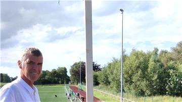 Ein Mann steht oberhalb eines Fußballplatzes und lächelt.