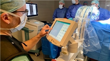 Ärzteteam an einem Operationstisch arbeitet mit einem mobilen Röntgen-C-Bogen, der kristallklar die Gefäße des zu operierenden Patienten auf einem Bildschirm darstellt
