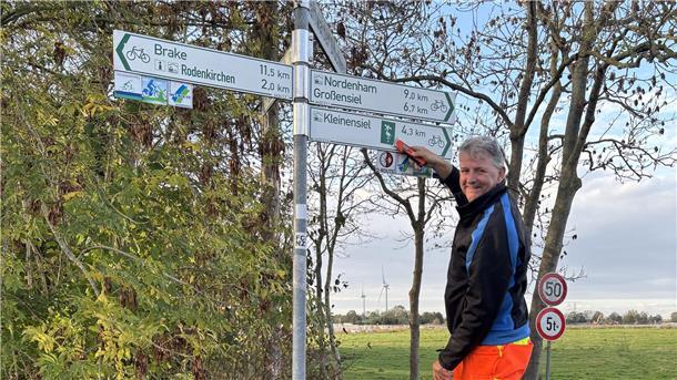 Holger Jacobs: Dank ihm bleiben Wesermarsch-Radler in der Spur Der Radwegewart Holger Jacobs steht auf einer Leiter und repariert ein Radwegeschild.