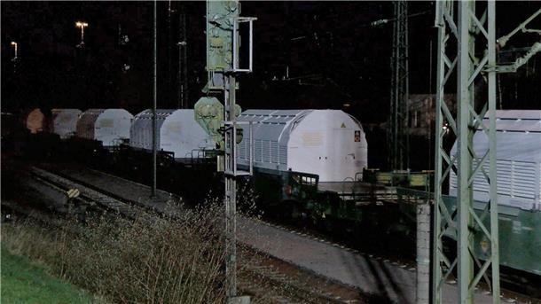 Ein Zug mit Castor-Behältern mit radioaktivem Atommüll rollt in der Dunkelheit über ein Bahngleis. 