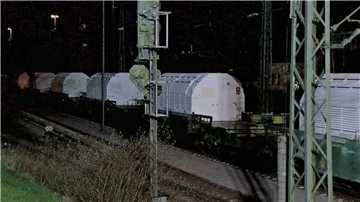 Ein Zug mit Castor-Behältern mit radioaktivem Atommüll rollt in der Dunkelheit über ein Bahngleis. 