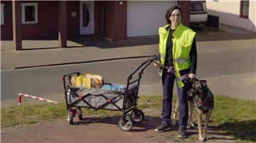 Frau in Warnweste mit Hund und Handwagen