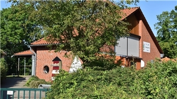 Ein Kindergartengebäude, davor Bäume und Büsche.