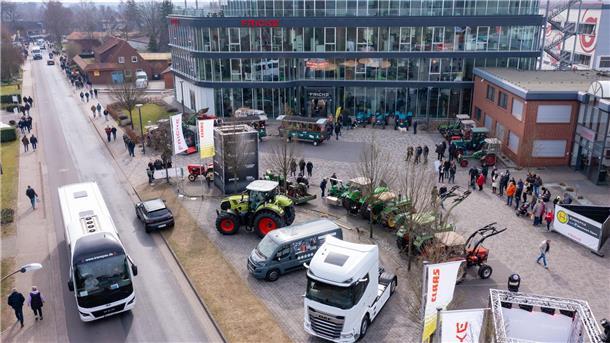 Eine Luftaufnahme von einem Firmengelände zeigt im Halbrund zur Präsentation geparkte Landmaschinen, Lkw und Nutzfahrzeuge. Besuchergruppen laufen zwischendurch.