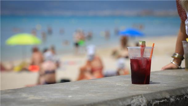 Ein rotes Getränk in einem Plastikbecher steht an einer Strandpromenade.