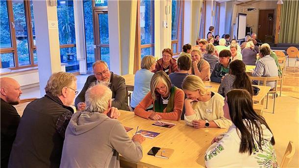 Menschen sitzen in Kleingruppen an mehreren Tischen verteilt.