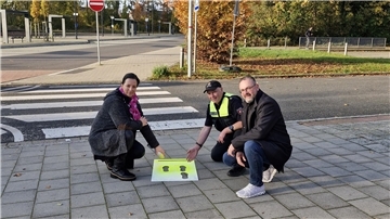Eine Frau und zwei Männer halten ein Plakat mit schwarzen Fußabdrücken auf gelbem Grund in die Kamera.