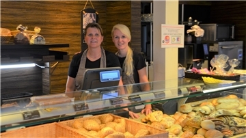 Zwei Frauen stehen hinter dem Bäckertresen und blicken in die Kamera. 