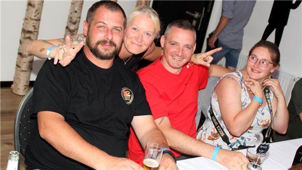 Vier Menschen feiern während der Blaulichtparty. Zwei Frauen und zwei Männer. Eine Frau umarmt zwei Männer und macht dabei mit ihren beiden Händen das Peace-Zeichen.