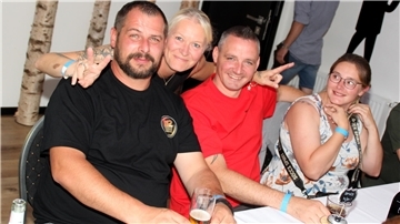 Vier Menschen feiern während der Blaulichtparty. Zwei Frauen und zwei Männer. Eine Frau umarmt zwei Männer und macht dabei mit ihren beiden Händen das Peace-Zeichen.