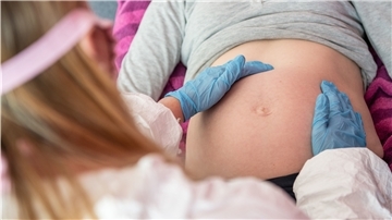 Eine Hebamme tastet den Bauch einer schwangeren Frau ab.