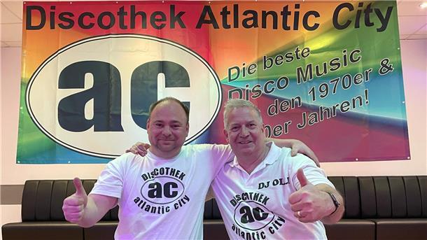 Zwei Männer strecken vor einem Banner mit der Aufschrift „Discothek Atlantic City" den Daumen in die Luft. Die DJs Markus Becker und Olli Hübler laden zur AC-Party ein. 