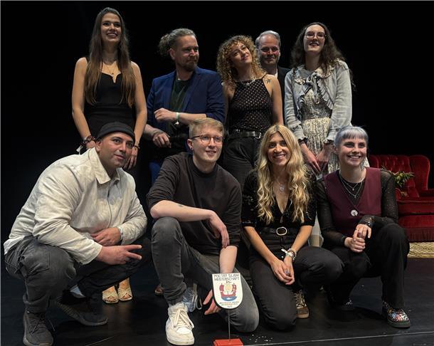 Finale mit Tiefgang: Matti Linke gewinnt Poetry-Slam-Meisterschaft Gruppenfoto der Teilnehmenden der niedersächsischen Poetry-Slam-Meisterschaft im Stadttheater Bremerhaven. Acht Personen stehen und knien auf der Bühne, in der Mitte ist die Siegerplakette zu sehen.