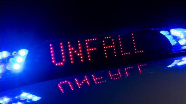 Das Blaulicht auf einem Fahrzeug der Polizei leuchtet in der Dunkelheit, während auf dem Display der Hinweis "Unfall" zu lesen ist.
