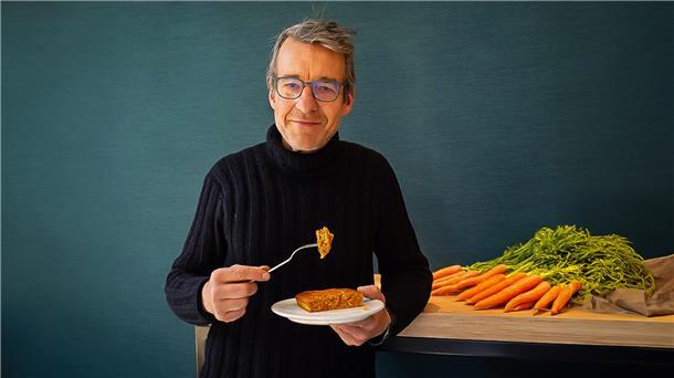 Ein Mann steht neben einem Haufen Möhren und isst einen Möhrenkuchen.  Frosta rettet Möhren und verwandelt sie in ein neues Produkt.
