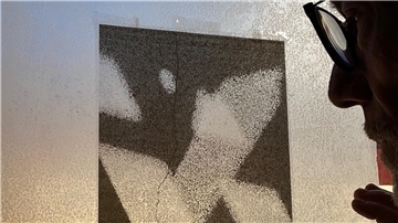 Ein Mann mit Brille betrachtet eine abstrakte Schwarz-Weiß-Grafik, die an einer mattierten Glasscheibe befestigt ist. Das Licht fällt durch das Glas und betont die Struktur des Bildes sowie das nachdenkliche Profil des Mannes.