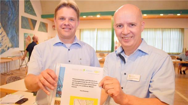 Das Foto zeigt zwei Männer, die eine Studie für ein interkommunales Gewerbegebiet in der Wesermarsch in der Hand halten. Die Studie empfiehlt die Gründung einer Gewerbepark-Gesellschaft. Um sie ging es jetzt im Wirtschaftsausschuss in Nordenham.
