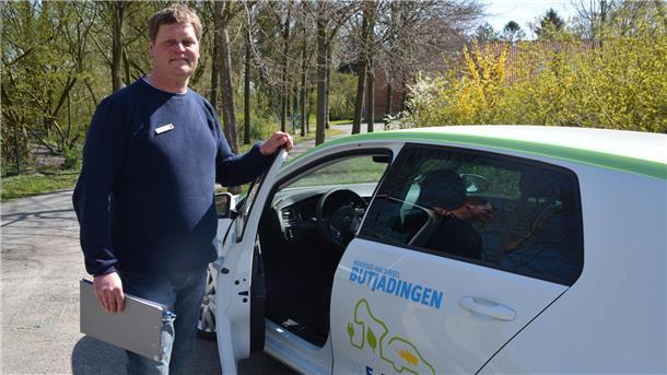 Ein Mann steht an einem Auto, bei dem die Fahrertür geöffnet ist.