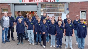 Eine Gruppe junger Menschen steht vor einem Feuerwehrgebäude 
