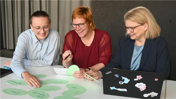 In Bremerhaven steht eine Taufe bevor: Name für den Hafenkran gefunden Drei Frauen schauen auf eine Auswahl.