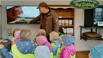 Kinder schauen auf einen Monitor. Ein Mann erklärt ihnen die Ernte. 