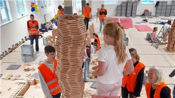 Kinder stehen vor einem Turm aus Holzbausteinen. Sie bauen in der Turnhalle Heeslingen eine Stadt.