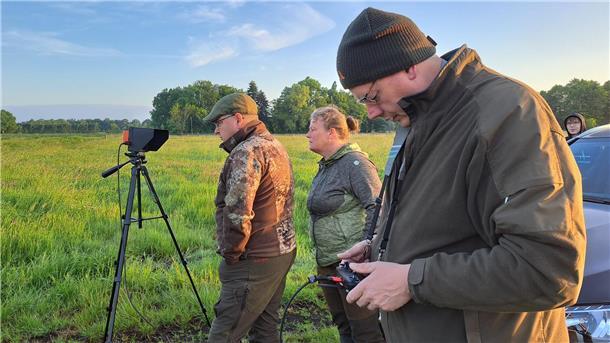 Die Kitzretter (v.l.) Jens Könighaus, Maike Voß und Ingo Bischoff verfolgen die Bilder der Wärmebildkamera, die die fliegende Drohne auf die Displays sendet.