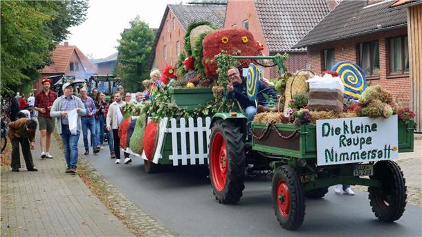 Vom Bieranstich bis zur Raupe Nimmersatt: Kassebruch feiert Erntefest Festlich geschmückter Erntewagen mit dem Motto „Die kleine Raupe Nimmersatt“ fährt durch eine Dorfstraße. Kinder in bunten Kostümen sitzen auf dem Wagen, viele Menschen laufen daneben. Im Hintergrund sind weitere Traktoren und Zuschauer zu sehen.