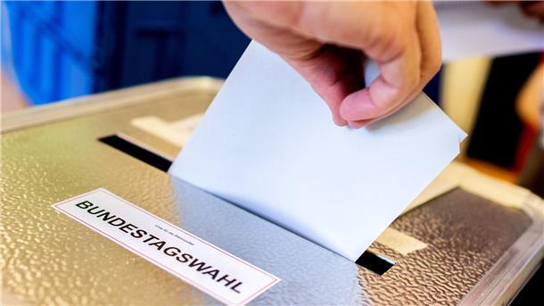 Jemand steckt seinen Stimmzettel in eine Wahlurne.