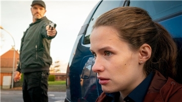 Die Kronzeugin Fiona (Marlene Tanczik) wird von einem Söldner (Christoph Domanski) mit einer Waffe bedroht.
