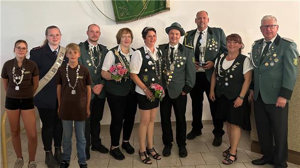 Mehrere Menschen stehen mit Orden und Blumen vor einer Vereinsfahne. 