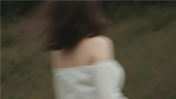 Eine junge Frau rennt in einem weißen Kleid durch den Wald. Das Bild ist verschwommen. Man erkennt de Frau schemenhaft von hinten.