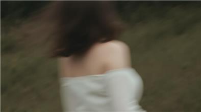 Eine junge Frau rennt in einem weißen Kleid durch den Wald. Das Bild ist verschwommen. Man erkennt de Frau schemenhaft von hinten.