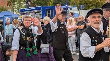 Männer und Frauen in Trachten winken in die Kamera.
