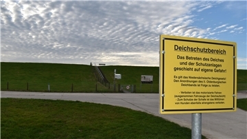 Bild von einem gelben Schild vor einem grünen Deich im Hintergrund