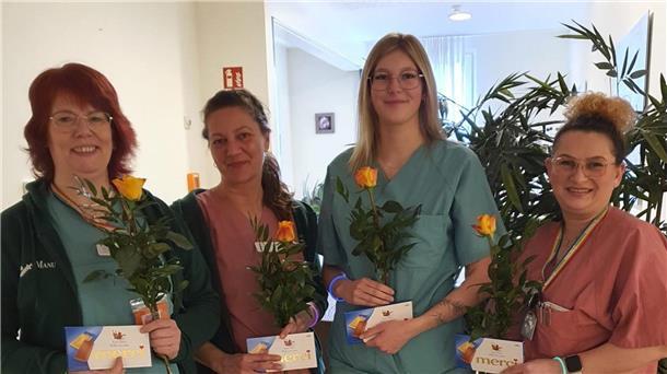 Vier Frauen stehen nebeneinander. Sie halten je eine Rose sowie Pralinen in den Händen.