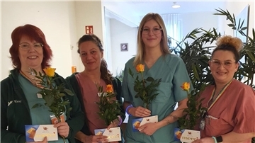Vier Frauen stehen nebeneinander. Sie halten je eine Rose sowie Pralinen in den Händen.