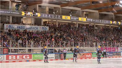 Drei Eishockey-Spieler stehen auf dem Eis. Oberhalb der Eisfläche sind neue Logen in der Eisarena Bremerhaven zu sehen.