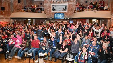 Eishockey-Fans schauen gemeinsam ein Spiel auf einer Leinwand und fiebern mit. 