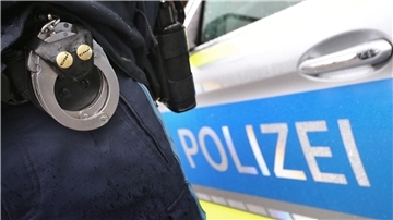 Ein Polizist mit Handschellen und einer Pistole am Gürtel steht vor einem Streifenwagen.