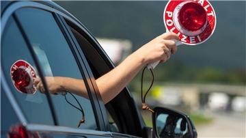 Bild von einem Auto, aus dessen Fenster eine Polizei-Kelle herausgehalten wird.