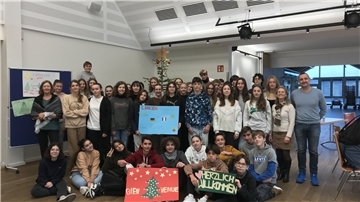 Teenager stehen für ein Gruppenbild in einem Raum. Die vordere Reihe sitzt. Es werden Schilder mit deutschen und französischen Texten zu Weihnachten hochgehalten.