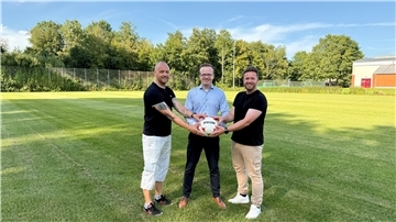 drei Männer auf einem frisch gemähten Fußballplatz halten einen Ball