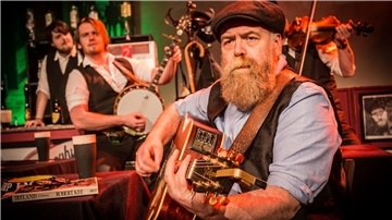 Ein bärtiger Mann mit Gitarre. Das Foto zeigt eine Szene aus der Show „Seven drunken Nights".