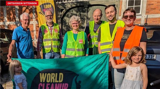 Einige Männer, Frauen und Kinder stehen nebeneinander und halten ein Transparent zum „World Cleanup Day“
