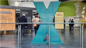 Besucher betrachten die Ausstellung „KLIMA_X“ im Klimahaus Bremerhaven. Im Vordergrund steht ein großes, türkisfarbenes X als zentrales Ausstellungselement.