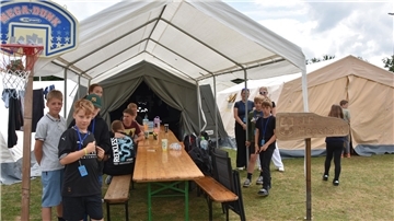 Eine Gruppe von Kindern und Jugendlichen steht in einem Zelt an einer Biertisch-Garnitur.