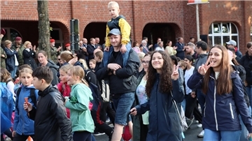 Eine Gruppe Menschen läuft vorbei, zwei Mädchen schauen in die Kamera. 